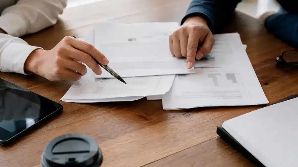 Manos de dos personas revisando documentos sobre un escritorio de madera cálida