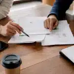 Manos de dos personas revisando documentos sobre un escritorio de madera cálida