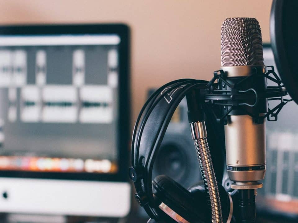 Micrófono de condensador con unos audifonos colgados, en un estudio de podcast